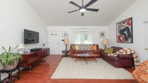 A living room with a flat-screen TV, a ceiling fan, a sofa set, a coffee table, and a potted plant. - Blue Rivers Cottage with Mountain Views (Afton)