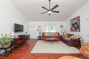 A living room with a flat-screen TV, a ceiling fan, a sofa set, a coffee table, and a potted plant. - Blue Rivers Cottage with Mountain Views (Afton)