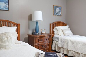 A hotel room with two single beds, a wooden nightstand with a lamp, and a framed picture on the wall.