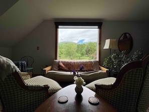 Una habitación acogedora con un gran ventanal, un sofá, dos sillones, una mesita con un jarrón y una lámpara.