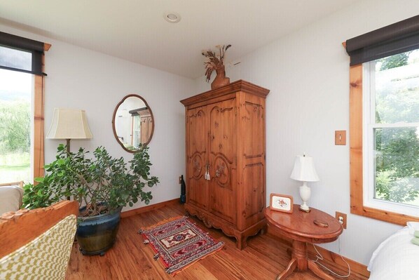 A room with a wooden cabinet, a mirror, a potted plant, a small table with a lamp, and a bed.