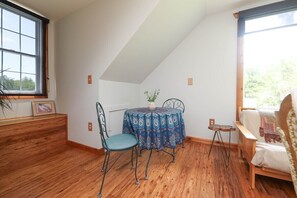 Une pièce avec un plafond en pente, une table à manger recouverte d’une nappe à motifs, une chaise, une petite table d’appoint et un lit avec une couverture.