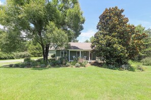 A single-story house with a front porch, surrounded by a well-maintained lawn and mature trees.