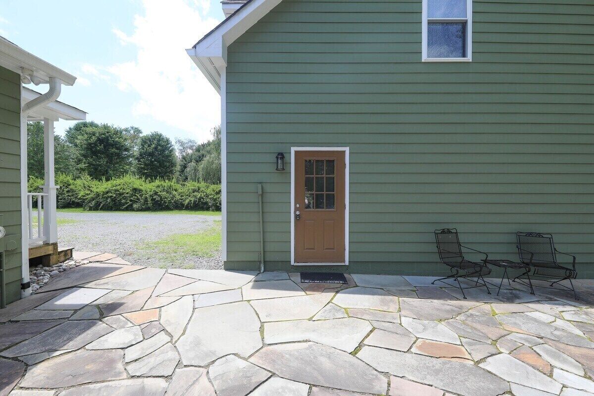 A house with a stone patio, a wooden door, and two metal chairs.