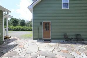 A house with a stone patio, a wooden door, and two metal chairs. - Blue Rivers Loft on the Brew Ridge Trail (Afton)