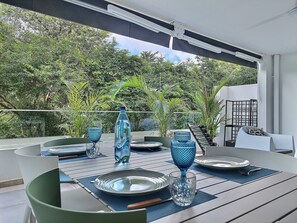 Un coin repas avec une table dressée pour deux personnes, entouré de verdure.