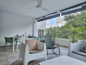 Un espace extérieur abrité, avec une table et des chaises, un ventilateur de plafond et une vue sur la verdure.