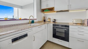 Una cocina moderna con armarios blancos, horno empotrado y ventana con vistas a un paisaje urbano.