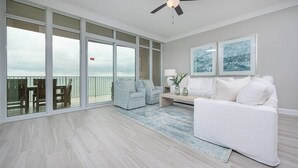 Un vaste espace de vie comprenant une grande porte-fenêtre coulissante donnant sur un balcon, un canapé blanc, un petit fauteuil et une table basse.