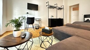A modern living room with a sofa set, a TV mounted on the wall, a plant on a side table, and a laundry rack.