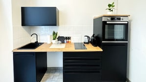 A compact kitchen with a black sink, a wooden countertop, a built-in oven, and a small potted plant.