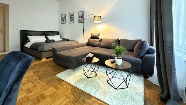 A modern living room with a sofa, a coffee table, a side table, a lamp, and a bed.