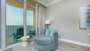 A balcony with a view of the ocean, a round grey sofa with cushions, a small white stool, and a floor lamp. - Phoenix Gulf Tower 1706 (Orange Beach)