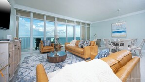 A spacious living room with a large window overlooking the sea, a dining area with a table and chairs, and a cozy seating area with a sofa and armchairs.