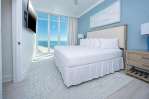 A bedroom with a large bed, a TV, a nightstand, and a view of the ocean. - Phoenix Gulf Towers Unit 1808 (Orange Beach)