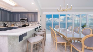 A modern kitchen with a large island, a dining area with a view of the ocean, and a chandelier. - Phoenix Gulf Towers Unit 2208 (Orange Beach)