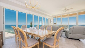 A dining area with a large table and chairs, a chandelier, and a view of the ocean. - Phoenix Gulf Towers Unit 2208 (Orange Beach)
