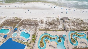 An aerial view of a beach resort with multiple swimming pools, a sandy beach, and a boardwalk. - Phoenix Gulf Towers Unit 2208 (Orange Beach)