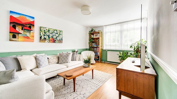 A living room with a sofa, coffee table, bookshelf, and a window with blinds. - GuestReady - Trendy 2Bed flat in East London (London)