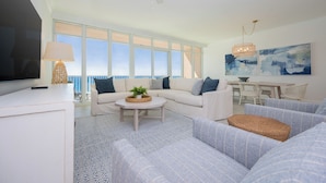 A spacious living room with a large window, a ceiling fan, a flat-screen TV, and a dining area with a table and chairs.