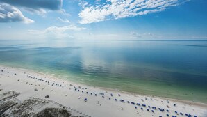 A beach with clear turquoise water, white sand, and numerous blue umbrellas.