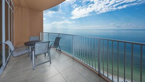 A balcony with a view of the ocean, a table, and two chairs.
