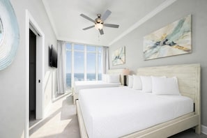A hotel room with a large bed, a ceiling fan, a TV, and artwork on the walls.