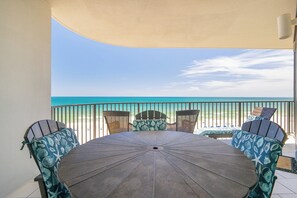 A covered patio with a table and chairs, a view of the beach, and a railing.