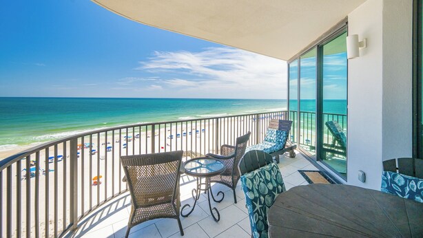 Un balcon avec vue sur la plage et l’océan, aménagé avec des fauteuils et une table en osier.