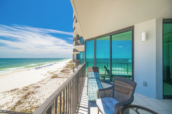 A balcony with a view of the beach and ocean, a wicker chair, and a glass table.