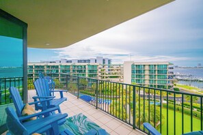 Un balcón con sillas azules, una piscina y vistas a edificios y al agua.