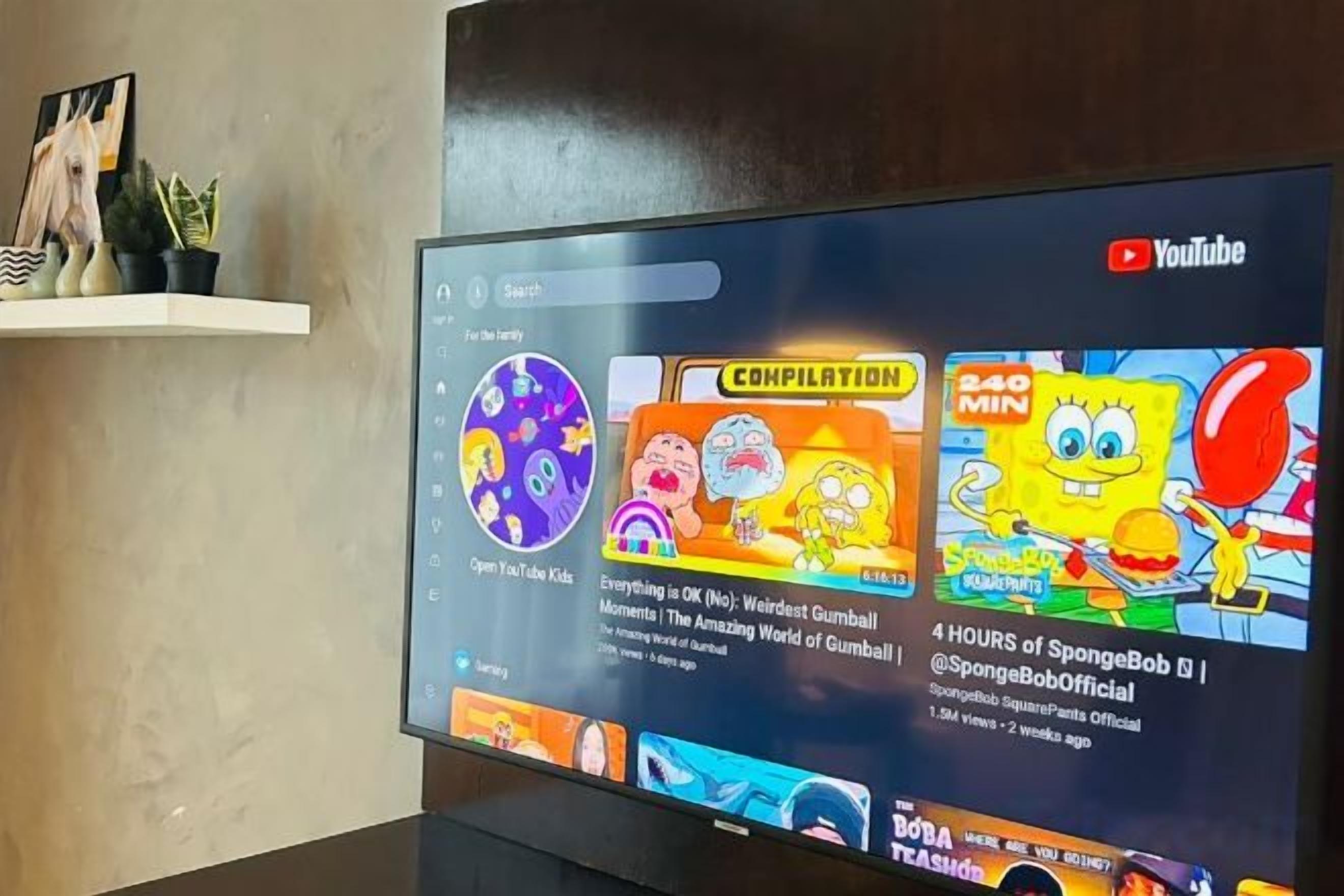 A YouTube interface on a flat-screen TV with a shelf above displaying decorative items.