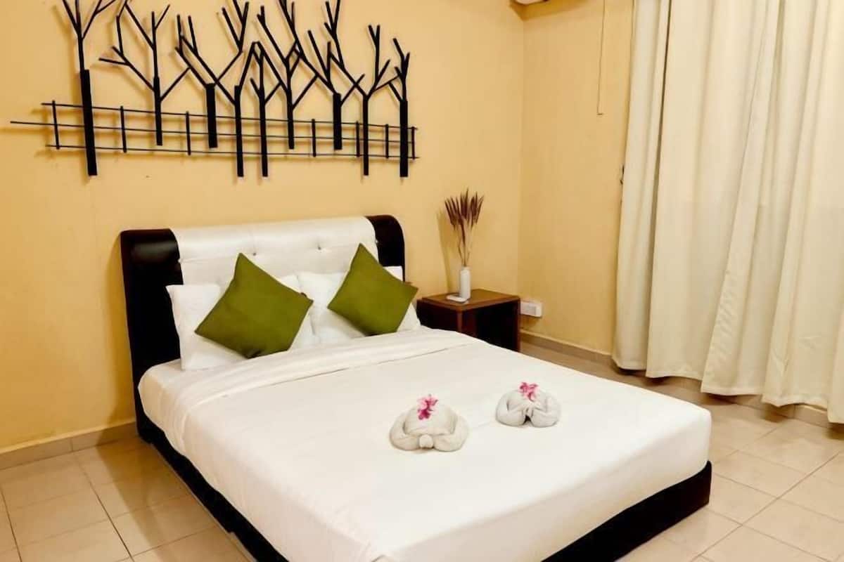 A neatly made bed with white bedding and green pillows, a wall-mounted tree decoration, a bedside table with a vase, and a window with curtains.