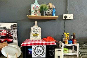 A kitchen area with a double-decker bus photo, a bottle of alcohol, and a small shelf with kitchen tools. - RHU DORMITORY LANGKAWI (Langkawi)