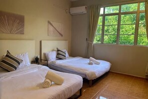 Ein Hotelzimmer mit zwei Betten, einem großen Fenster mit Blick auf Grünflächen und einer Wand-Klimaanlage.