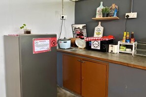 A kitchen with a refrigerator, a microwave, a sink, and a countertop with various items including a plant, a bottle, and a framed picture. - RHU DORMITORY LANGKAWI (Langkawi)