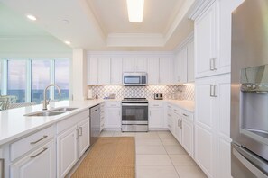 A modern kitchen with white cabinetry, stainless steel appliances, and a large window providing a view. - In the heart of Orange Beach - Phoenix Orange Beach II 1701 (Orange Beach)