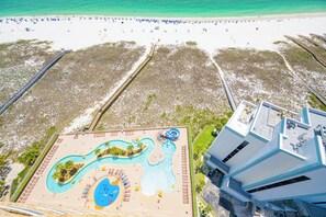 An aerial view of a resort with a large pool area, a beach, and a modern building.