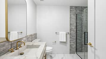 Un baño moderno con lavamanos de mármol, accesorios dorados, cabina de ducha de vidrio y inodoro blanco.