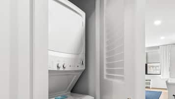 Un lavadero con lavadora y secadora blancos, una puerta con picaporte de latón y un tapete azul en el suelo.