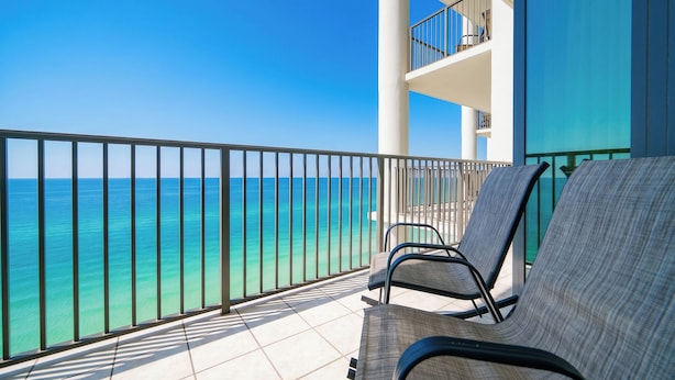 A balcony with a view of the ocean, a railing, and a few chairs.