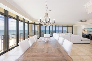 Een ruime eetruimte met een lange houten tafel, beklede witte zitplaatsen en een kroonluchter.