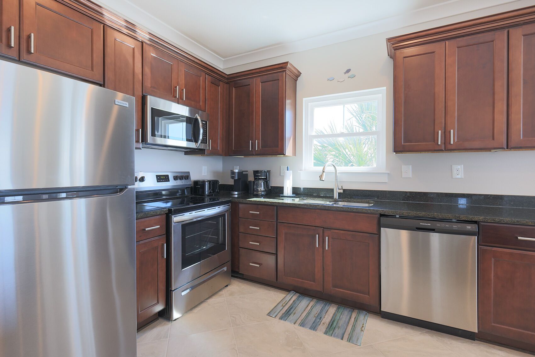A modern kitchen with stainless steel appliances, wooden cabinets, and a window providing natural light.