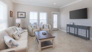 A modern living room with a beige sofa, two armchairs, a wooden coffee table, a TV on the wall, and a grey console table. - Serene Gulf-front Retreat in Fort Morgan (Gulf Shores)