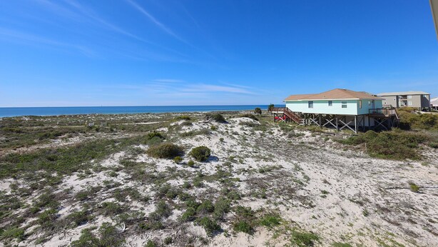 A beach house with a sandy landscape and a clear blue sky. - Serene Gulf-front Retreat in Fort Morgan (Gulf Shores)