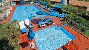 A resort with two swimming pools, sun loungers, umbrellas, and a view of the sea. - Residence La Filanda in Costermano With Pool (Costermano sul Garda)
