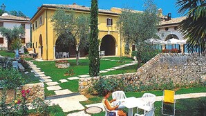 A courtyard with a yellow building, stone pathway, and outdoor seating area. - Residence La Filanda in Costermano With Pool (Costermano sul Garda)