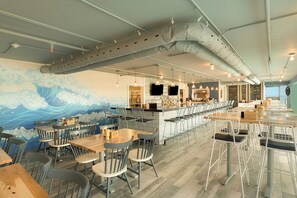 A restaurant with a wave-themed mural, multiple seating areas, and a bar counter.