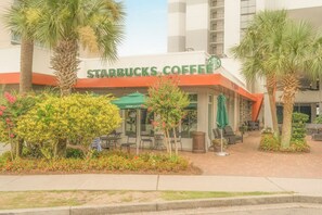 A Starbucks Coffee with outdoor seating, surrounded by palm trees and flowering plants.