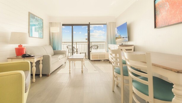 Habitación de hotel con balcón, sofá, mesa de comedor y sillas.